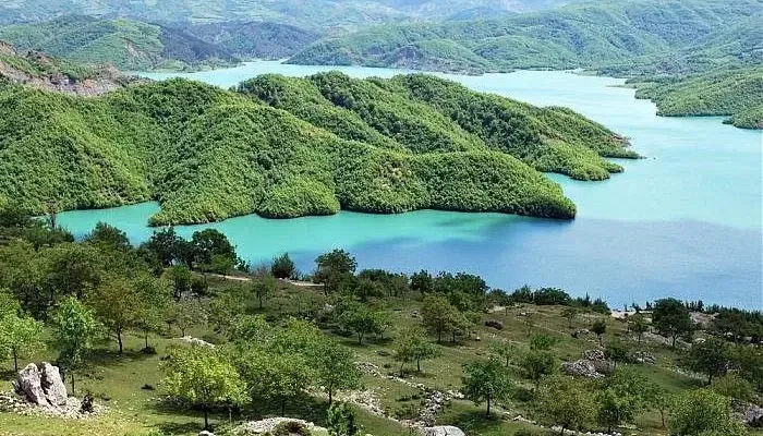 A pastoral landscape of green hills and the calm waters of Lake Bovilla, with the foothills approaching the historic town of Krujë.