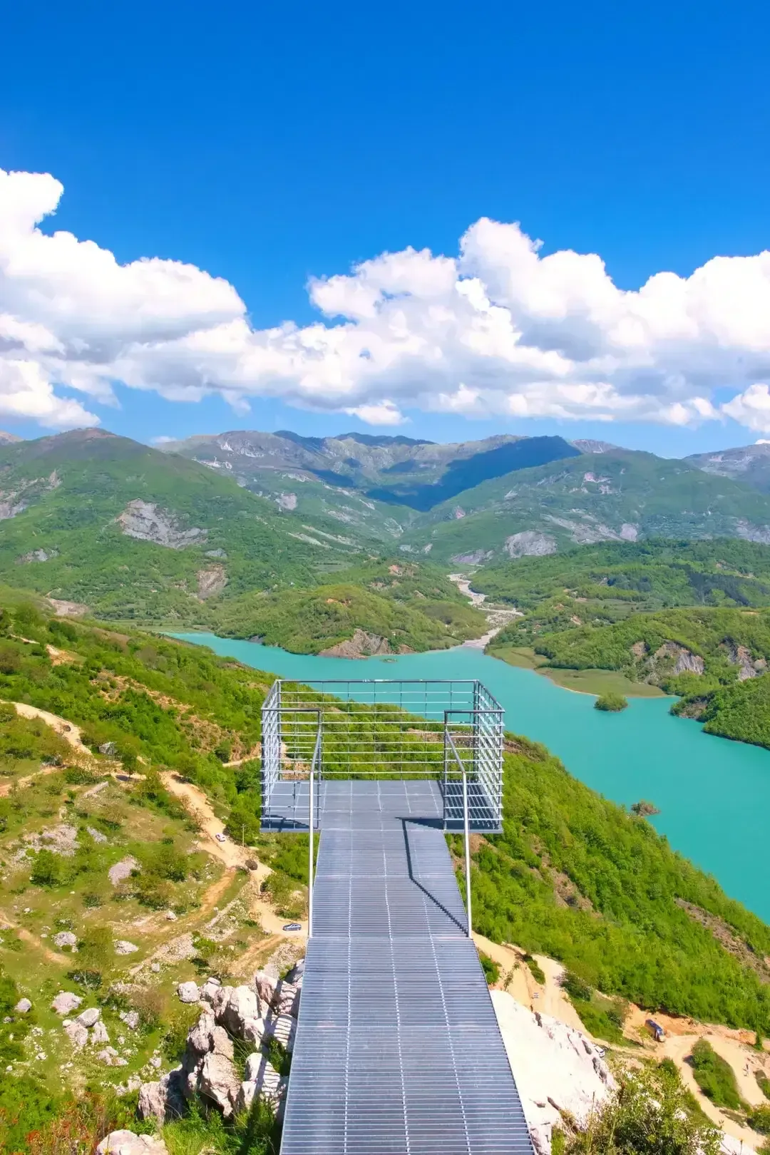 The metal viewing deck extending out from the cliff above Lake Bovilla, with the reservoir and Dajti mountains beyond.